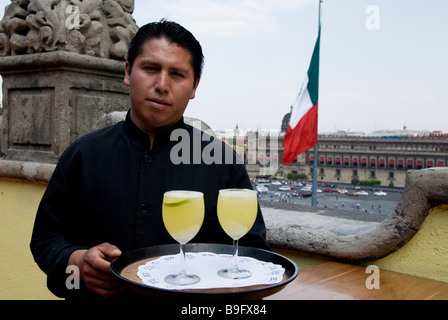 eine mexikanische Kellner servieren Margarita mit Blick auf die Plaza De La Constitución und mexikanische Flagge, Mexico City, Mexiko Stockfoto