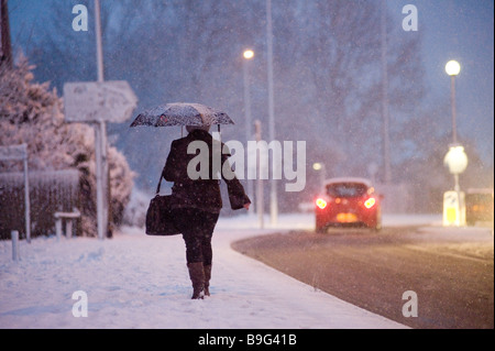 Lady Heimweg von der Arbeit entlang einer schneebedeckten Fahrbahn an einem Winter-Abend in england Stockfoto