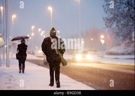 Menschen, die zu Fuß zur Arbeit entlang einer schneebedeckten Fahrbahn an einem Winter-Abend in england Stockfoto