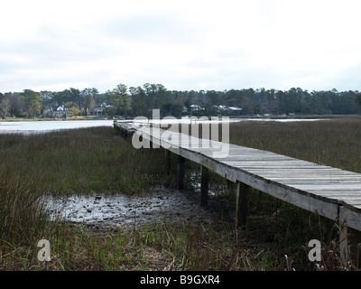 Ansicht von Marsh Fluss Creek und langes Boot dock vom Ufer in niedrigen Perspektive mit Details von Grass Holzbohlen Stockfoto