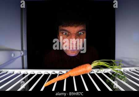 Mann über eine einzelne Karotte in einen leeren Kühlschrank Stockfoto