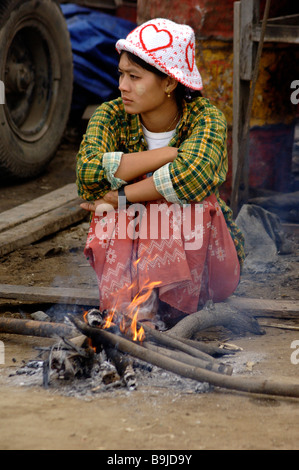 Birmese Frau sitzt auf einem kleinen Feuer an einem kalten Morgen im Fährhafen von Mandalay Myanmar Stockfoto