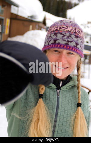 Eine Frau mit blonden Zöpfen geht an eine Skihütte mit Skiern auf die Schulter. Stockfoto