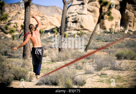 Ein Mann nutzt seine Arme um Gleichgewicht beim Seil zu Fuß oder Slacklining zwischen zwei Bäumen in der kalifornischen Wüste. Stockfoto