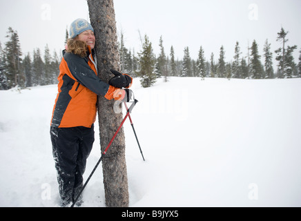 Eine junge Frau schmiegt sich an einen Baum in einem schneebedeckten Feld im Winter in Bend, Oregon. Stockfoto