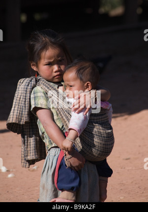 In einem kleinen Dorf zwischen Luang Prabang und Phonsavan trägt ein kleines Mädchen ein Baby in einem Papoose über ihre Brust. Stockfoto