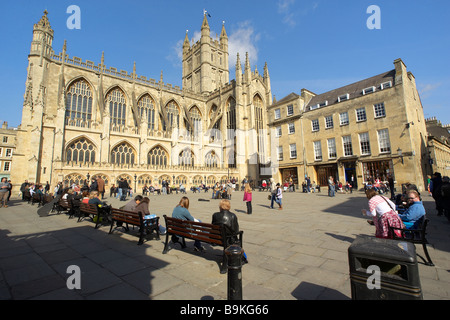 Leute sitzen in der Sonne beobachten ein Straßenmusikant außerhalb Bath Abbey in Bath durchführen somerset uk. Stockfoto