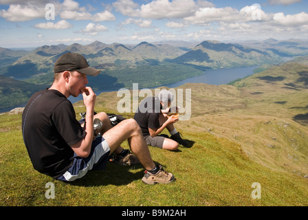 Wanderer beim Mittagessen und bewundern Sie die Aussicht vom Gipfel des Ben Lomond an einem sonnigen Tag, Stirlingshire, Schottland Stockfoto