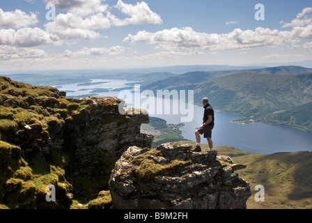 Ein Wanderer schaut auf die atemberaubende Aussicht vom Gipfel des Ben Lomond an einem sonnigen Tag, Stirlingshire, Schottland Stockfoto