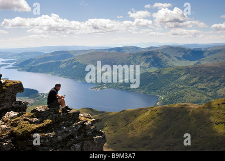 Ein Wanderer schaut auf die atemberaubende Aussicht vom Gipfel des Ben Lomond an einem sonnigen Tag, Stirlingshire, Schottland Stockfoto