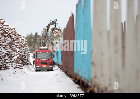 Laden von Logs von Log LKW zu Ladung Log Zug im Winter auf Eisenbahndepot, Finnland Stockfoto