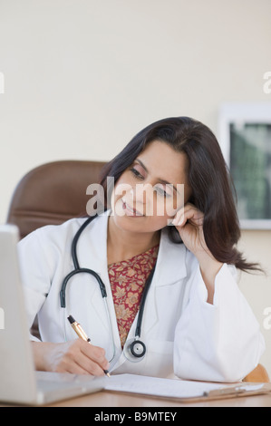 Ärztin mit einem Laptop und Schreiben von Notizen Stockfoto