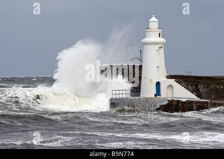 Wellen brechen über die Mauer und den Leuchtturm am Eingang des Macduff Harbour, Schottland, UK. Stockfoto