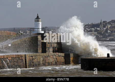 Wellen brechen über die Mauer und den Leuchtturm am Eingang der Hafen von Banff, Schottland, UK. Stadt von Macduff ist im Hintergrund Stockfoto