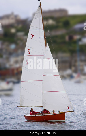 Troy Klasse Segelboot in Fluss Fowey Mündung Köpfen heraus zum Meer mit der Cornish Stadt Polruan im Hintergrund. Stockfoto