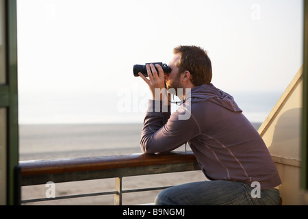 Junger Mann, Blick durch ein Fernglas vom Balkon, breite Haven Stockfoto