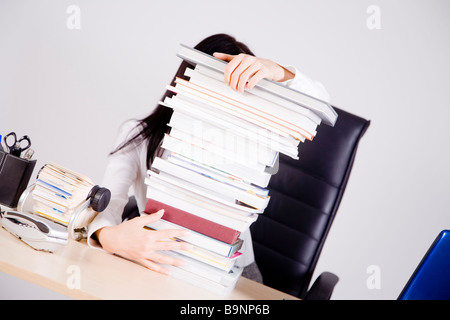 Geschäftsfrau auf Schreibtisch versteckt hinter Stapel Bücher Stockfoto