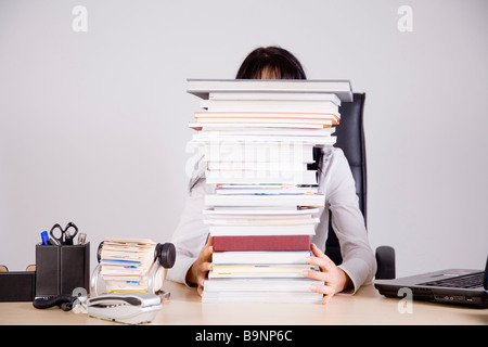 Geschäftsfrau auf Schreibtisch versteckt hinter Stapel Bücher Stockfoto
