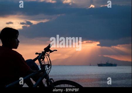 Ein Junge, den Sonnenuntergang in der Bucht von Manila aus Roxas Bulevard Stockfoto