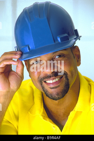 Afrikanische amerikanische Mann trägt blaue Bau Bauarbeiterhelm lächelnd, als er Helm Tipps. Stockfoto