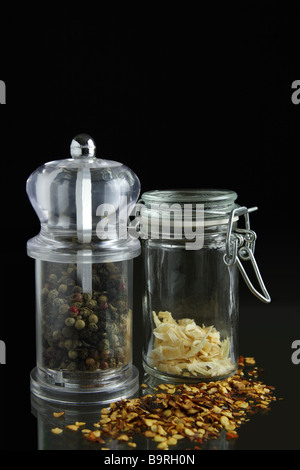 Pfeffermühle und Glas mit verstreuten Gewürz auf schwarzem Hintergrund Stockfoto
