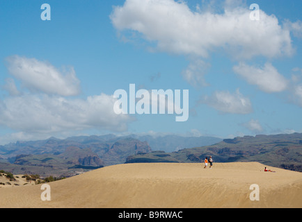 Touristen zu Fuß auf den Dünen in Maspalomas mit den Bergen von Gran Canaria in der Ferne Stockfoto