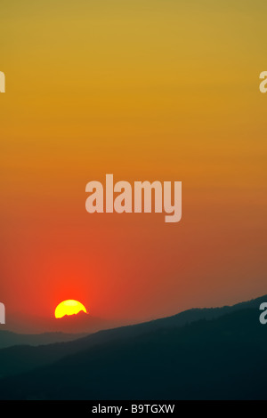 Intensive entfernten Sonnenuntergang über die Silhouetten der Wappen von eine Reihe von Bergen Stockfoto