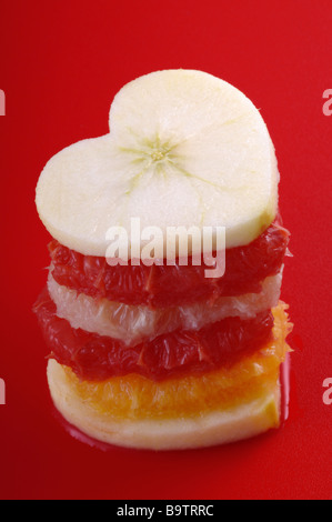 Haufen von Früchten in Form von Herzen auf rotem Grund Stockfoto