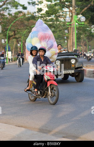 Junges Paar transportieren eine große Plastiktüte gefüllt mit aufgeblasenen Luftballons auf ein Motorrad in Hanoi Vietnam Stockfoto