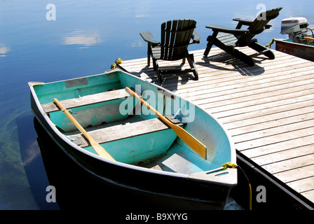 Zwei hölzerne Adirondack Stühle auf einem Boot dock auf einem See noch mit Himmel Reflexion Stockfoto