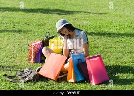 Junge Frau im Park, umgeben von Einkaufstaschen Stockfoto
