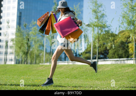 Junge Frau läuft durch den Park, mehrere Einkaufstaschen tragen Stockfoto