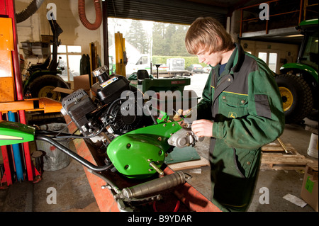 Ein junger Lehrling tragen Overalls Overalls arbeiten auf die Reparatur von eines John Deere Rasenmähers in der Garage-Werkstatt, UK Stockfoto