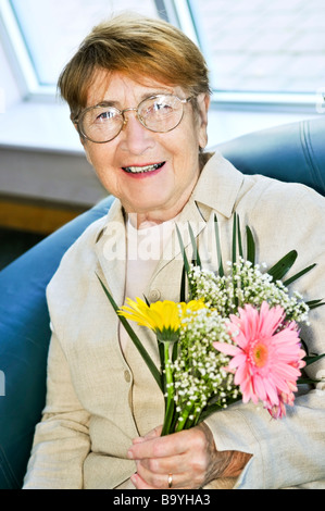 Ältere Frau mit Brille Blumen halten und Lächeln Stockfoto
