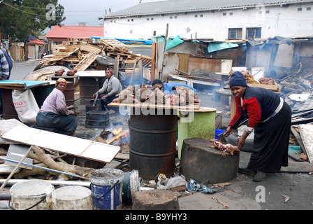 Drei Arbeiter der Dame rösten ein Schaf Kopf und Vorbereitung andere als eine lokale Spezialität, Township Langa, Cape Town, Südafrika Stockfoto