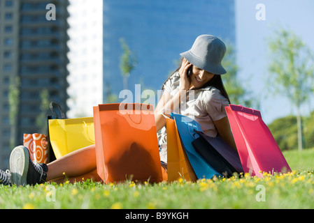 Junge Frau sitzt am Boden umgeben von Einkaufstaschen, reden über Handy Stockfoto