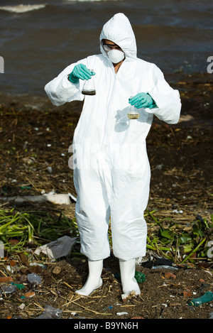 Person im Schutzanzug hält Fläschchen gefüllt mit verschmutztem Wasser Stockfoto