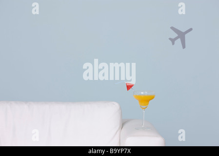 Cocktail am Arm des Sofas, Flugzeug-Form im Hintergrund Stockfoto