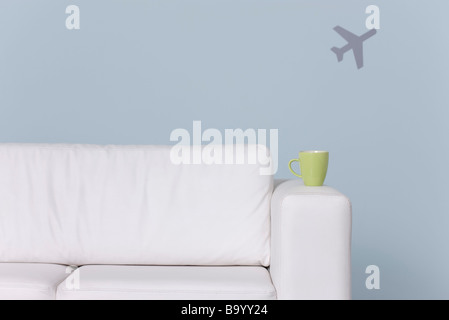 Becher am Arm des Sofas, Flugzeug-Form im Hintergrund Stockfoto