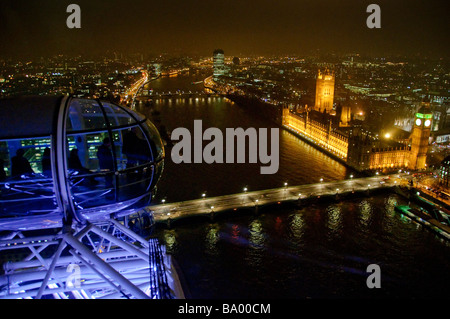 LONDON, Vereinigtes Königreich – Ein nächtlicher Blick von der Spitze des London Eye mit Blick auf die beleuchteten Parlamentshäuser und die Themse. Die ikonische Architektur des Palace of Westminster, einschließlich des Elizabeth Tower (allgemein bekannt als Big Ben), hebt sich vom dunklen Himmel ab, der sich im Wasser der Themse spiegelt. Stockfoto