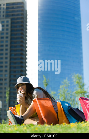 Junge Frau im Park mit Einkaufstüten, trinken mit Strohhalm Stockfoto