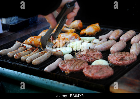 Ein Mann dreht Hacksteaks, Wurst und Hähnchen immer auf einen Gas-Grill gekocht Stockfoto