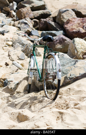 Ein altes grünes Fahrrad lehnt sich gegen einen Stein an einem Sandstrand warten auf seine oder ihre Besitzer zurück nach Hause zu nehmen Stockfoto