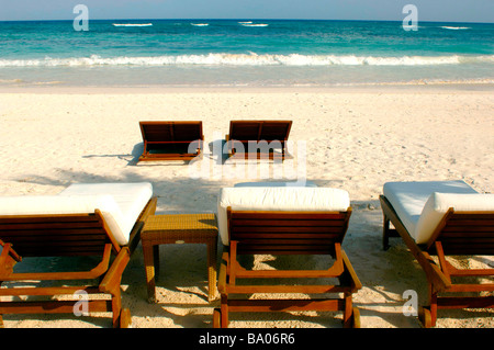 Liegestühle und Schirme an einem tropischen Strand mit schönen weißen Sand, blaues Wasser und brechenden Wellen. Stockfoto