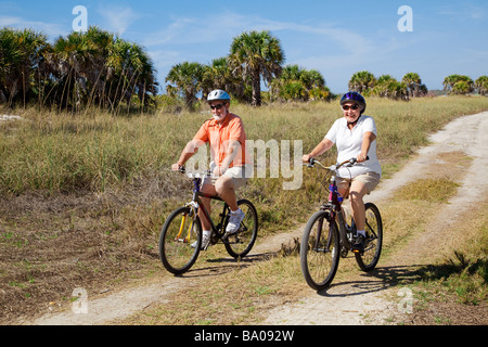Älteres Paar am Strand tragen Helme und Sonnenbrillen Radfahren Stockfoto