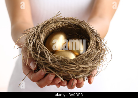Hände halten Nest mit goldenen Eiern Stockfoto