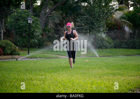 junge Frau läuft durch Sprinkler System um sich abzukühlen Stockfoto