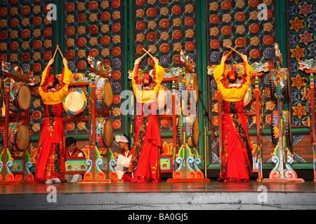 Drei Koreanerinnen in leuchtendem Gelb und rot Kleider auf der Bühne spielen traditionelle Folkore Trommeln "oh-Go-Mu" Stockfoto