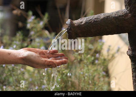 Frau wäscht den Schmutz aus der Hand mit Wasser aus einer alten Eisen-Pumpe. Stockfoto