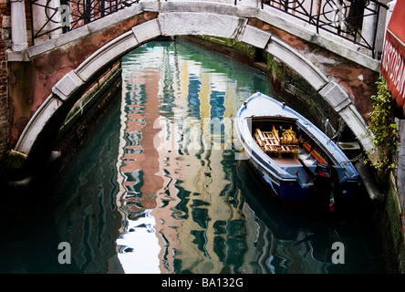 Motorboot unter der alten venezianischen Brücke mit Gebäuden, die sich im Kanalwasser in Venedig, Italien, widerspiegeln Stockfoto